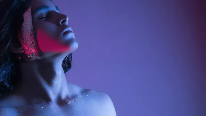 Rostro de perfil con los ojos cerrados bajo luz roja de una mascarilla LED