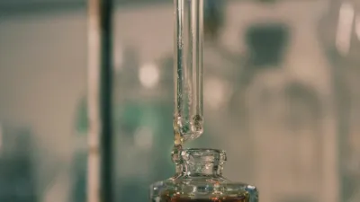 Pipeta de vidrio sobre un frasco con sérum ámbar en un laboratorio, con el fondo desenfocado